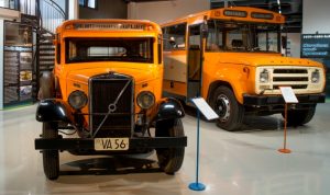 Kaksi oranssia nokkamallista postibussia, vanhempi 30-luvulta ja taka-alalla amerikkalaisen koulubussin näköinen postibussi 80-luvulta.