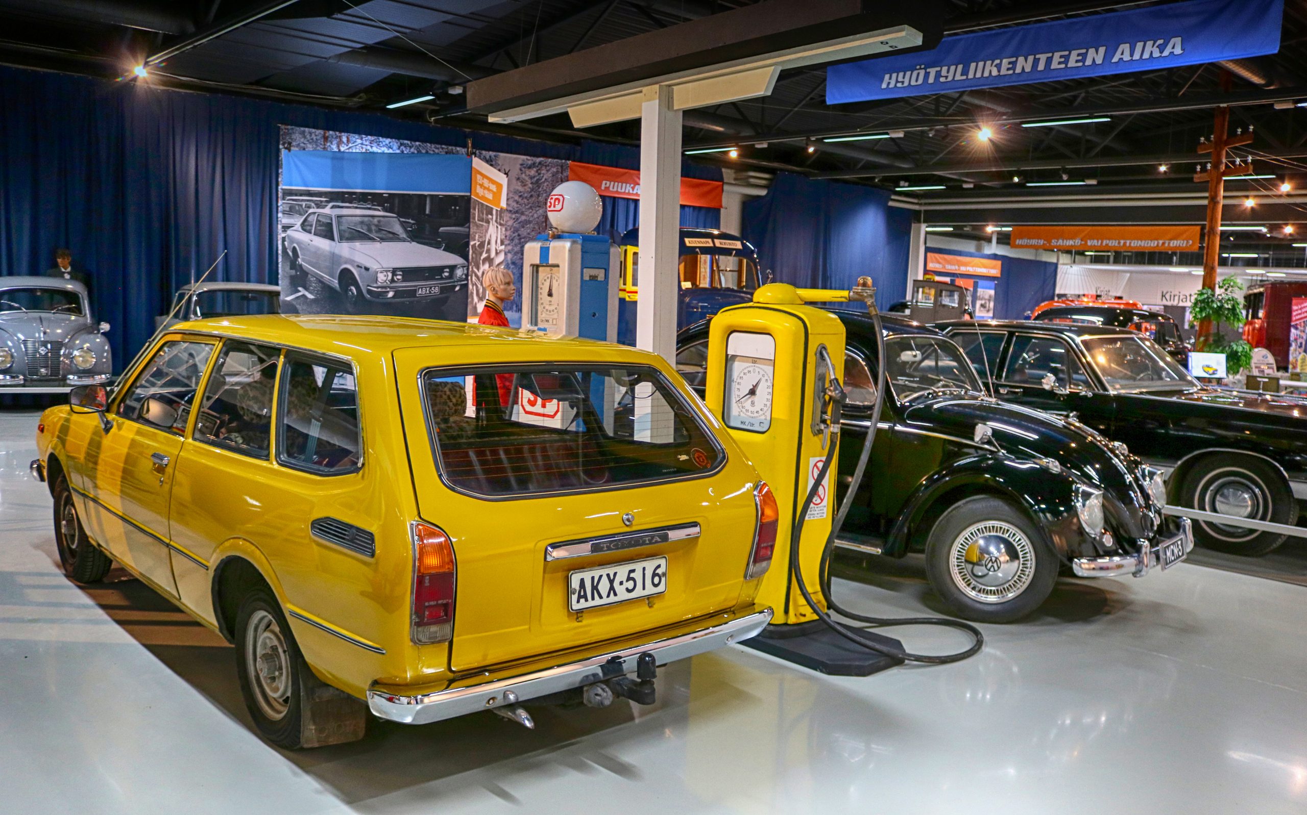 Keltainen farmari-Corolla 70-luvulta ja musta Kupla 60-luvulta tankattavana bensamittareiden edessä Mobilian Tankit täyteen -näyttelyssä.