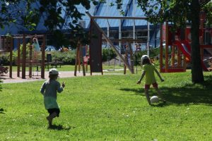 Lapset pelaavat jalkapallolla Mobilian nurmikkoalueella leikkipuiston edessä.