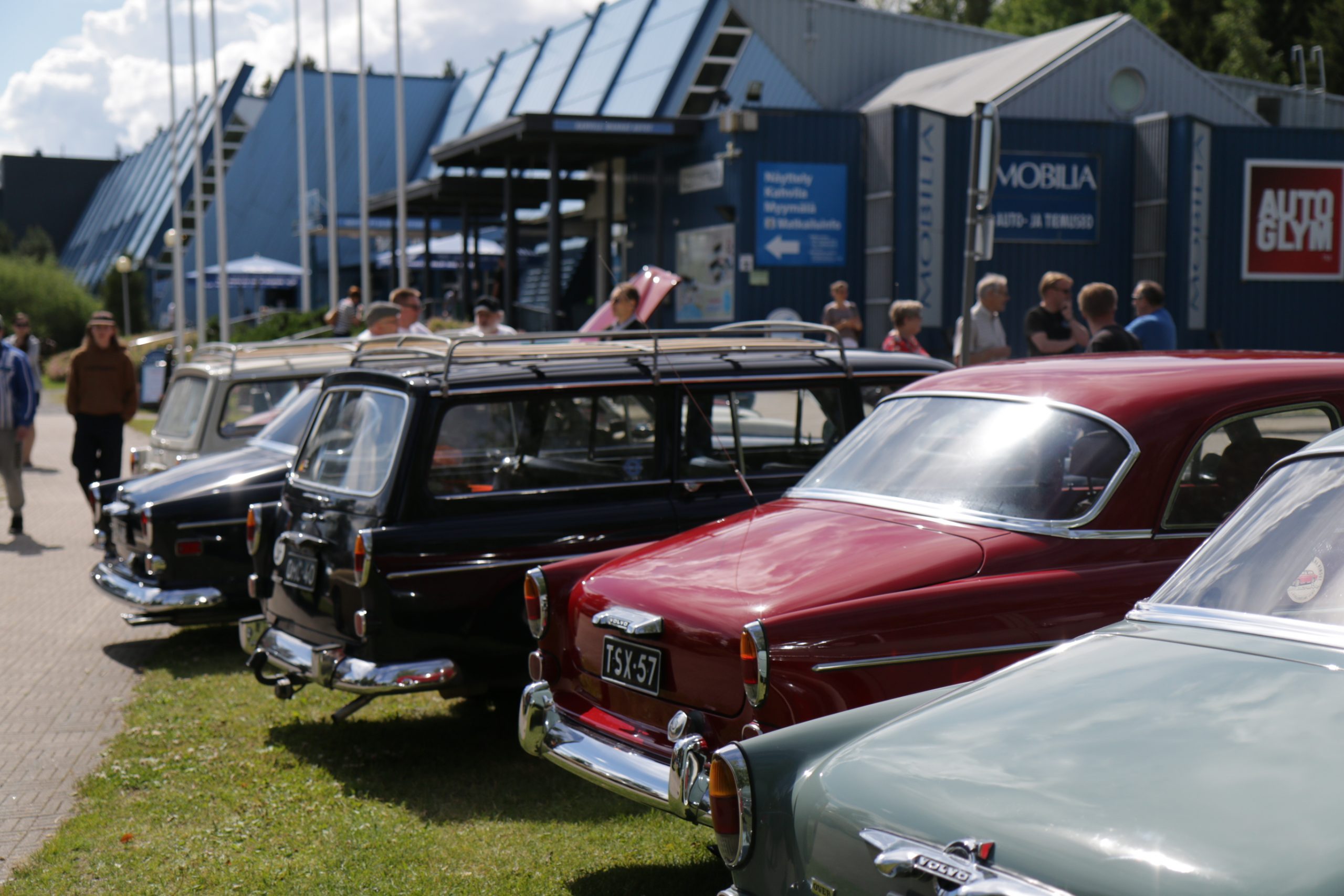 Mobilian Keskustalon edessä parkissa vanhoja Volvoja, joista kuvassa takaosat. Harmaan ja punaisen sedan-mallin takaa näkyy tumma farmarivolvo.