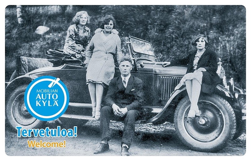Vanhassa mustavalkokuvassa auton lokasuojan ja astinlaudan päällä istuu ja seisoo poseeraamassa tyylikkääsit pukeutuneet kolme naista ja yksi mies.