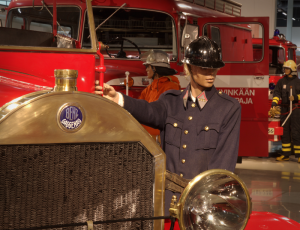Vanhan paloauton nokka ja palomiehen uniformuun ja kypärään puettu mallinukke.