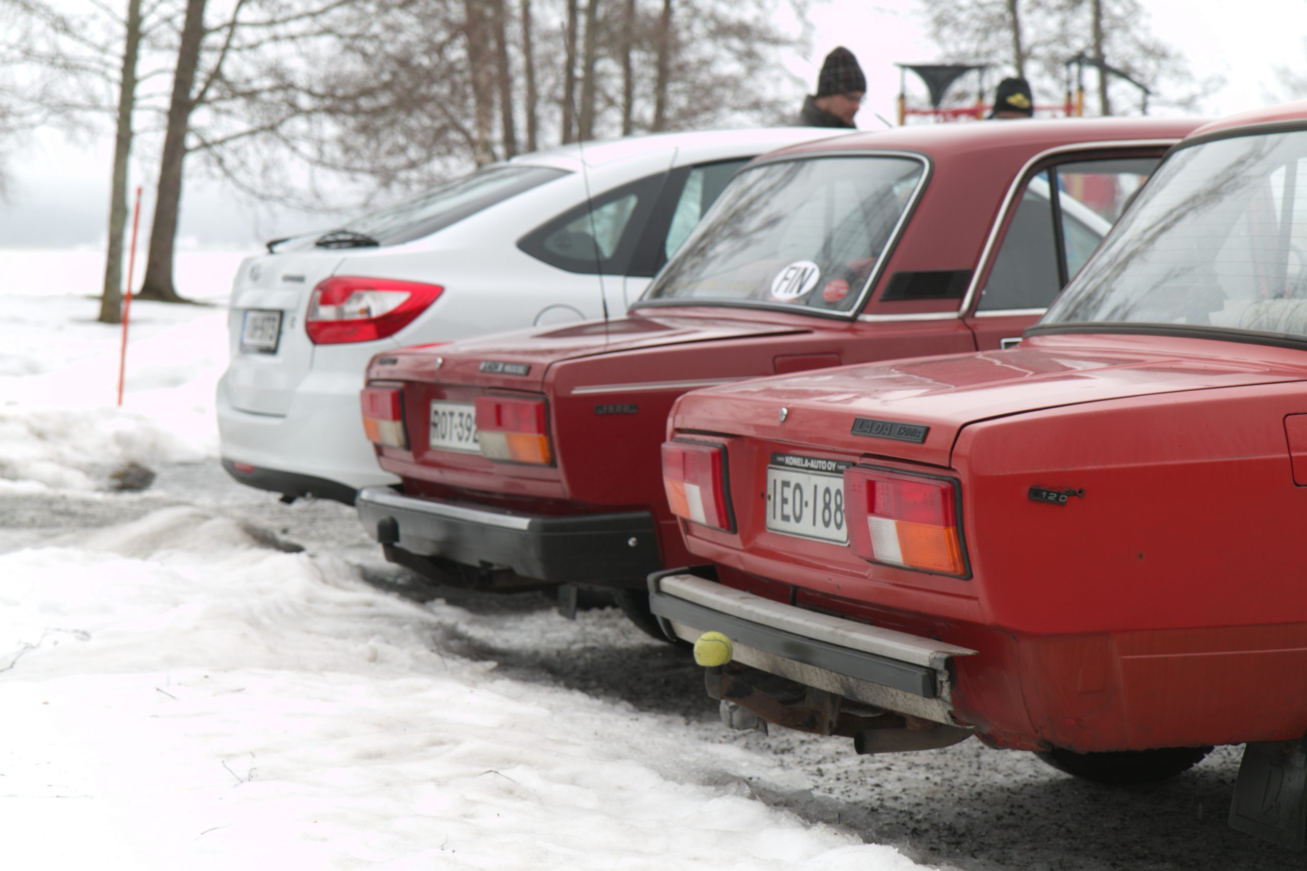 Lumisella parkkialueella kaksi punaista vanhaa Ladaa sekä yksi uudempi auto.