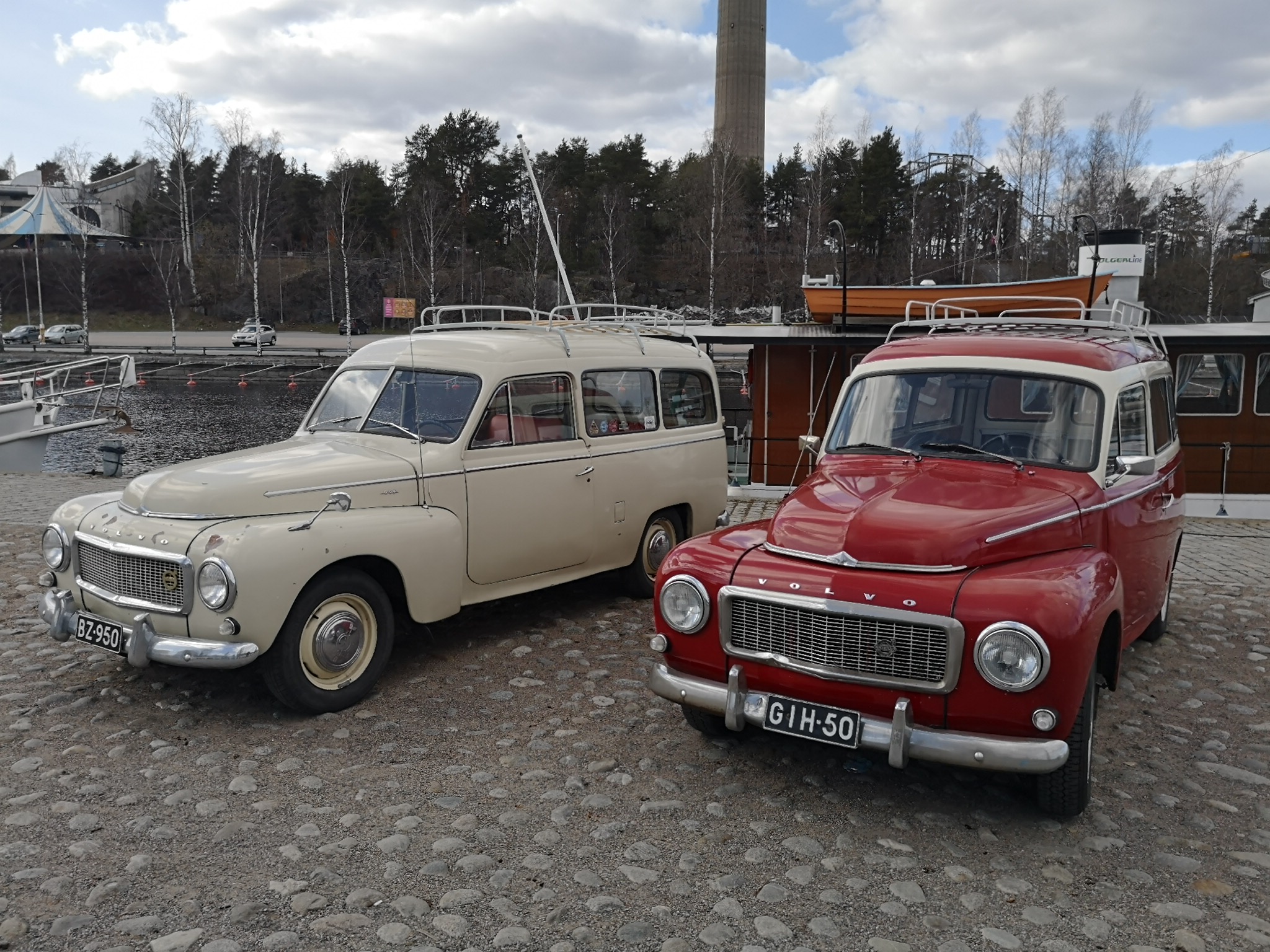 Valkoinen ja tummanpunainen PV-Volvo kuvattuna etuviistosta mukalakivisella satama-alueella.