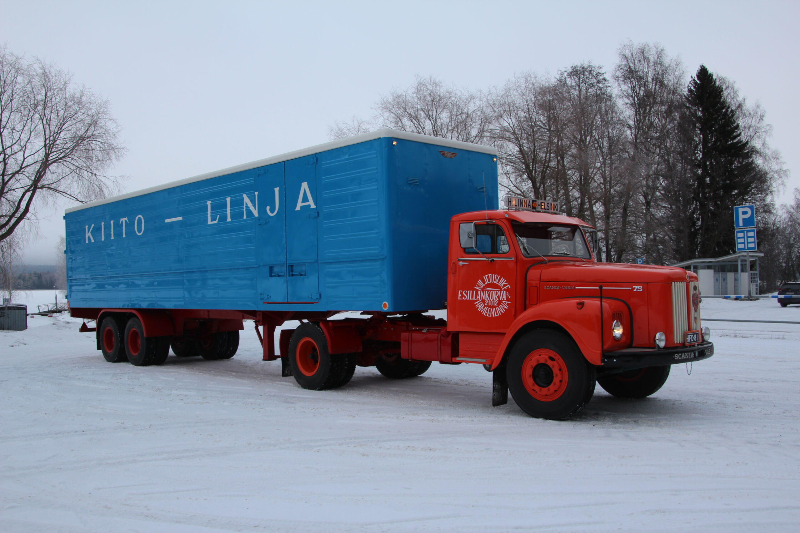 Vanha nokkamallinen Scania-Vabis lumisella pihalla kuvattuna. Auton hytti on kirkkaan punainen ja perävaunu on sininen valkoisella Kiito-linja-tekstillä.