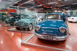 Tummansininen Panhard 1960-luvun alusta on keulan muotoilulta melko pyöreä. Auto kuvattu näyttelyhallissa vierellään aikakauden villapaitaan puettu naisnukke. Taustalla näkyy muita näyttelyn ajoneuvoja.