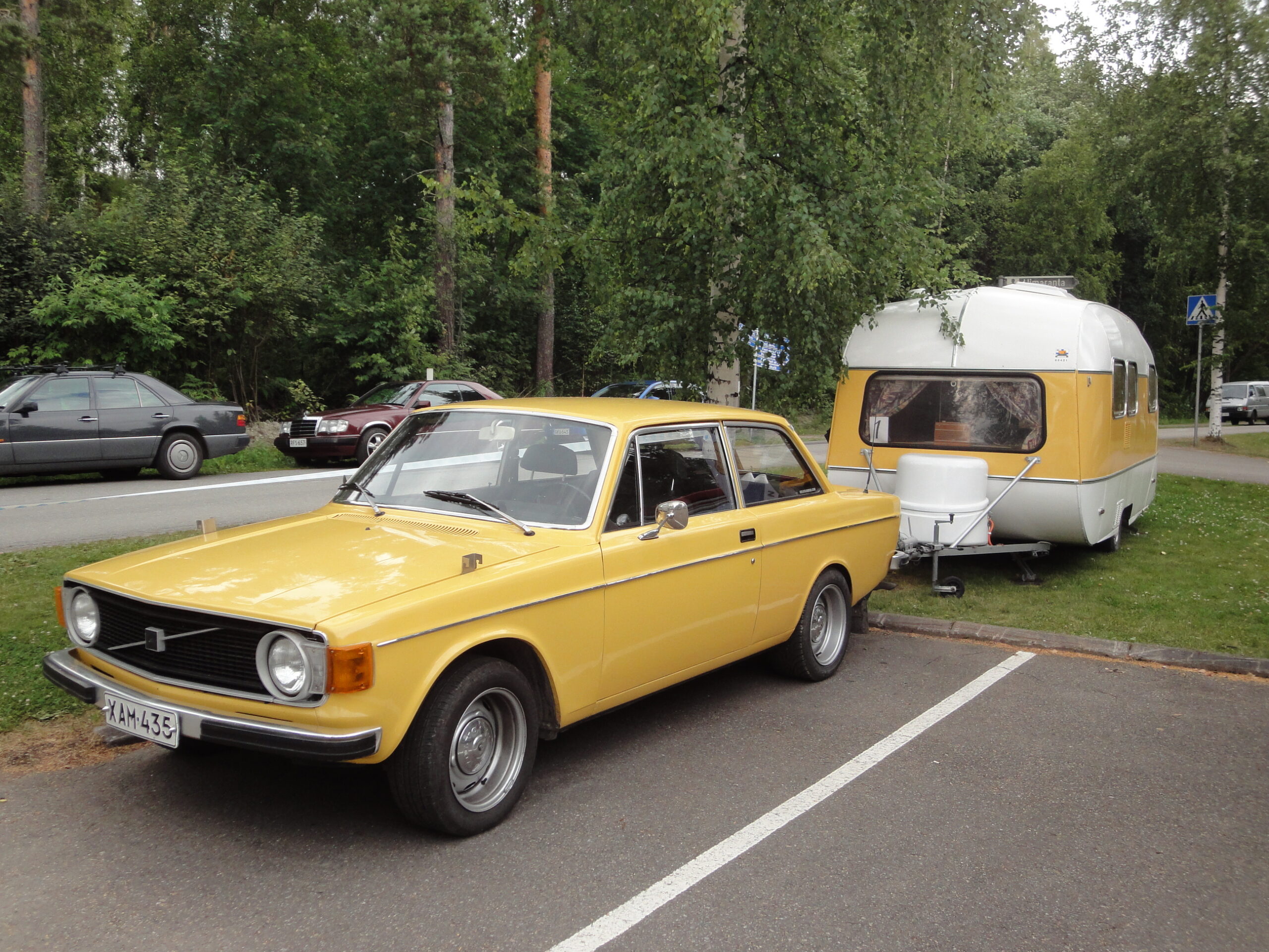 keltainen Volvo ja matkailuvaunu parkkiruudussa.