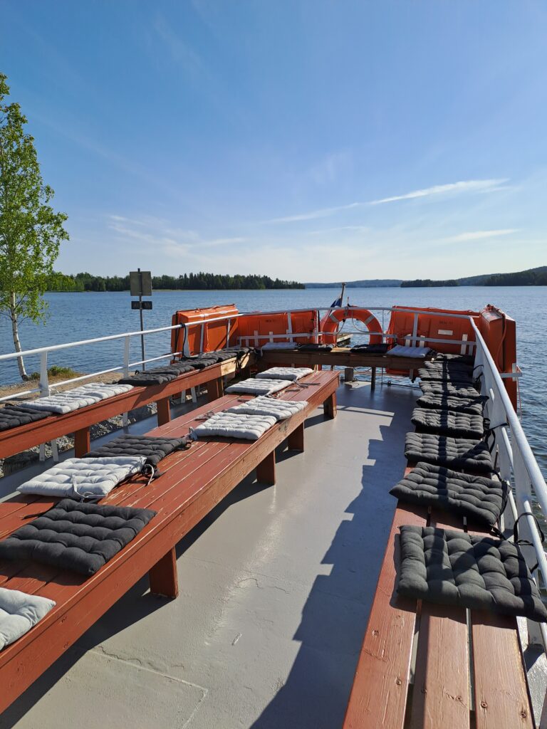 Laivan kannen istuimet ja taustalla aurinkoinen järvimaisema