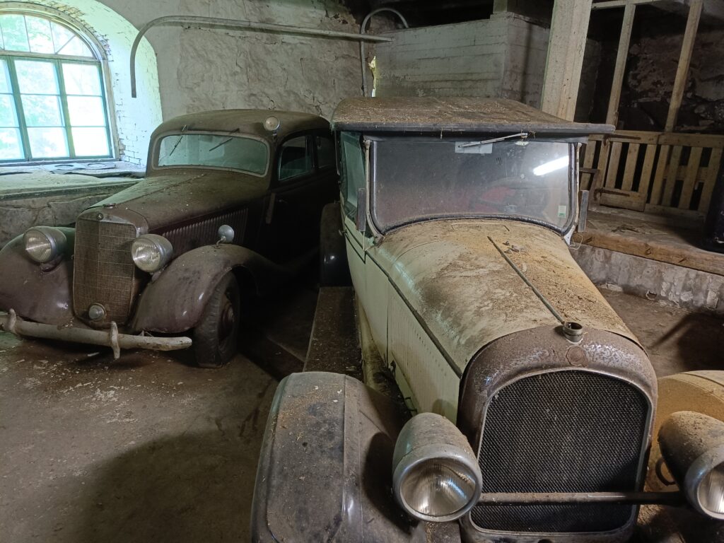 Vanhassa navetassa kuvattu kaksi vanhaa autoa paksun pölynpeittäminä.